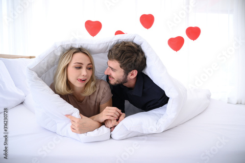 Attractive young man and women are in bed under the blanket with very warm atmosphere.