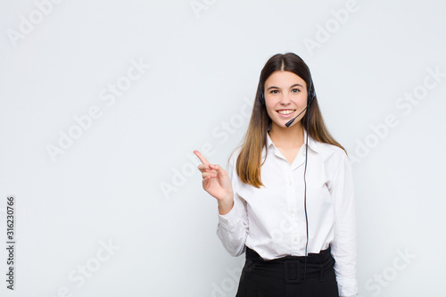 young pretty woman smiling cheerfully, feeling happy and pointing to the side and upwards, showing object in copy space with headphones and microphone