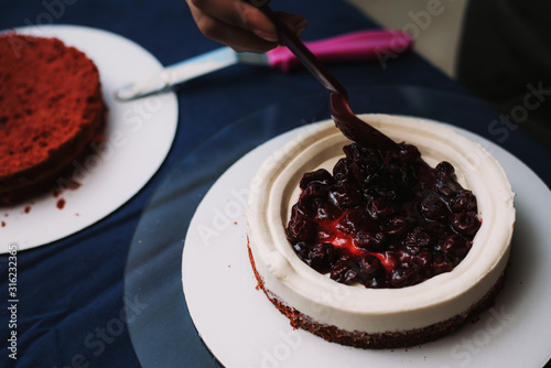 Cook puts jam with berries on the cake with cream. The pastry chef puts the jam and decorate the cake photo