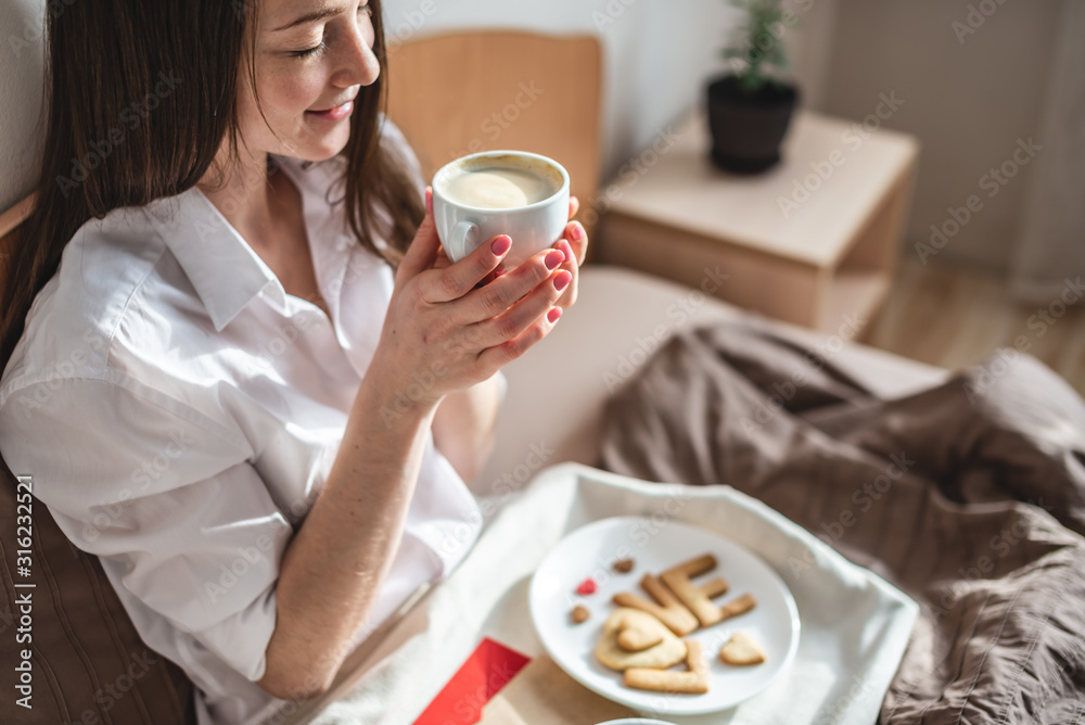 Young woman have a romantic Breakfast in morning bed. Coffee and word love from cookies. Surprise on Valentine's day Young woman have a romantic Breakfast in morning bed. Coffee and word love from cookies. Surprise on Valentine's day