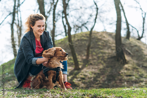 Candid photo of attractive young curly woman with her brown cocker spaniel posing in the park