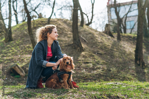 Attractive young curly woman with her brown cocker spaniel posing in the park