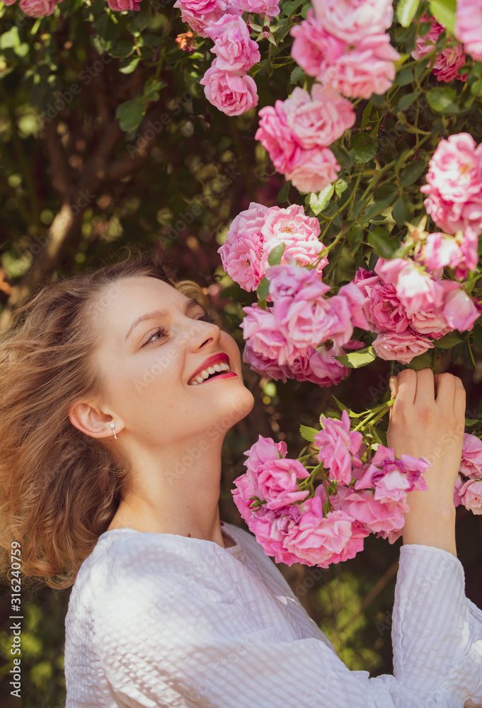 Fototapeta premium Pink rosebush blooming. Happy woman walking at rose garden. Relaxing and happiness concept. Young smiling girl enjoys pink rose flowers. Flowers of pink rose.