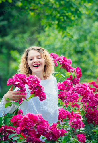 Young smiling woman surrounded rose flowers. Tender girl enjoing summer time and roseblush blossom. Rosier concept. Pink summer flowers blossom. Happy woman holding roses.