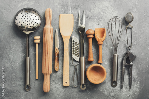 Flat lay kitchen tools and utensils on a gray concrete background, toned. Top view. Kitchenware is metal and wood.