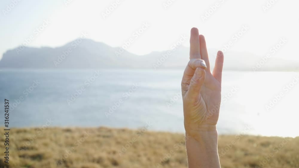 Group of senior people doing yoga exercises at nature. Detail shot, part view woman rising arm with gyan mudra sacral hindu gesture while staying in trikanasana pose against bright sky Group of senior people doing yoga exercises at nature. Detail shot, part view woman rising arm with gyan mudra sacral hindu gesture while staying in trikanasana pose against bright sky