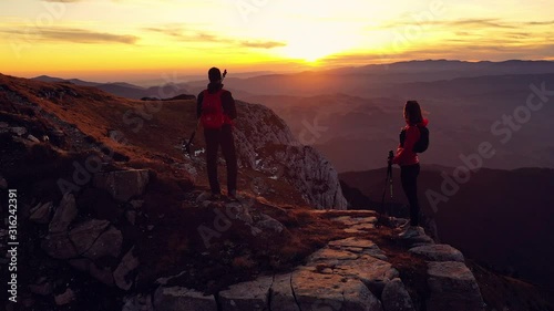 Aerial 4k drone clip with couple of hikers watching a beautiful sunset on top of Bucegi mountain ridge, during magical golden hour light in autumn season, in Romania