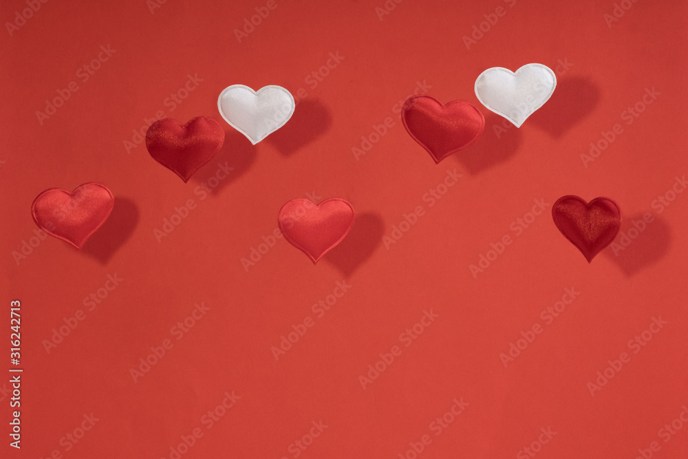 2 white and 5 red flying small textile hearts and their shadows are on a background of red velvet paper.