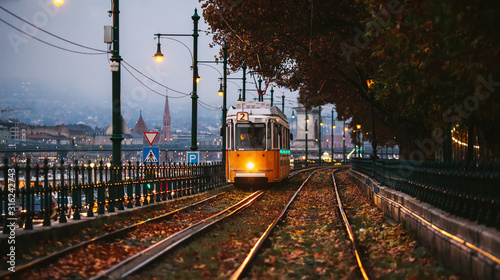 A yellow tram travels on route number 2 along the banks of the Danube. Cloudy autumn evening in Budapest.