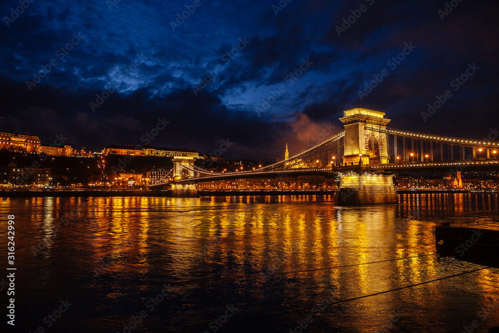 Night View Of Szechenyi Bridge. Famous Chain Bridge Of Budapest. Beautiful lighting and reflection in the Danube River.