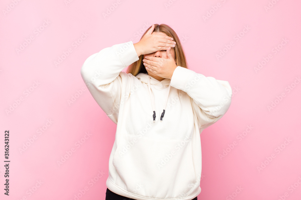 young blonde woman covering face with both hands saying no to the ...