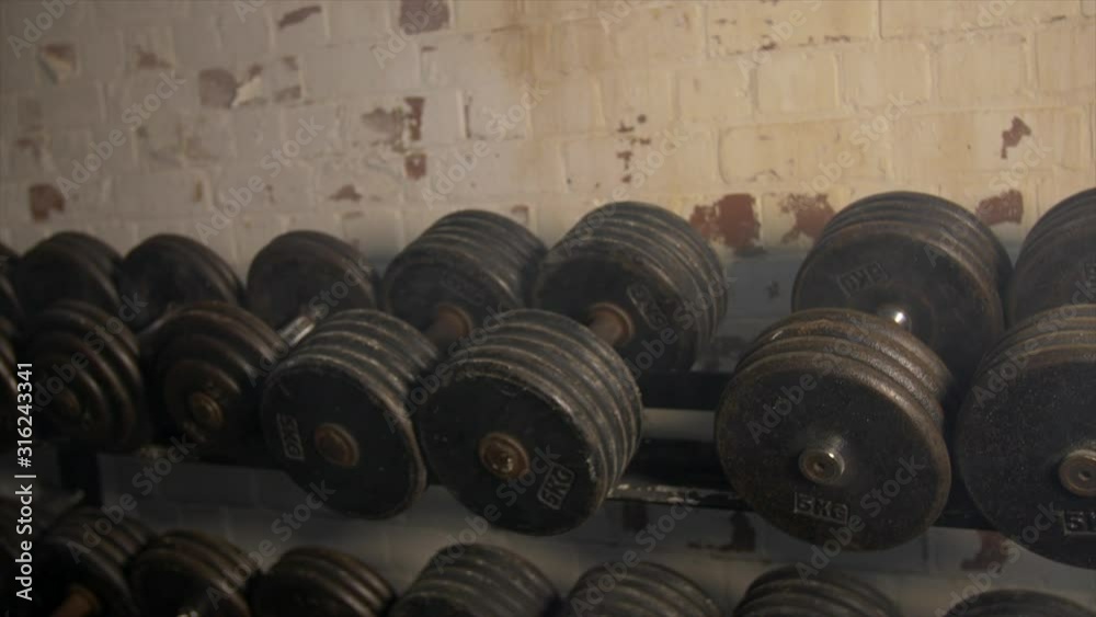 Pan Across Of Weights Lined Up On Weight Rack In Industrial Gym Old Style Old Fashioned Under Ground Gym. Paint Work Scratched Off