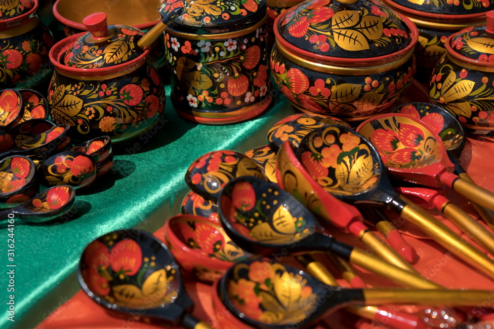 Souvenir painted wooden spoons and caskets with floral patterns lie on red with green shiny material.