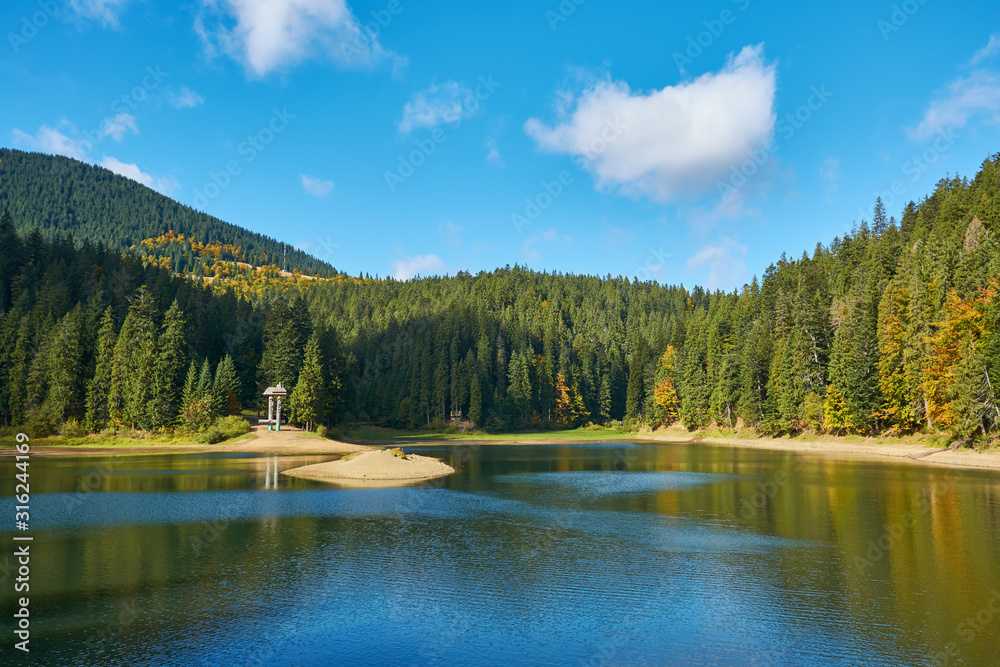 View of Synevir high-altitude lake by autumn day. The leaf fall forest, lake and mountains.