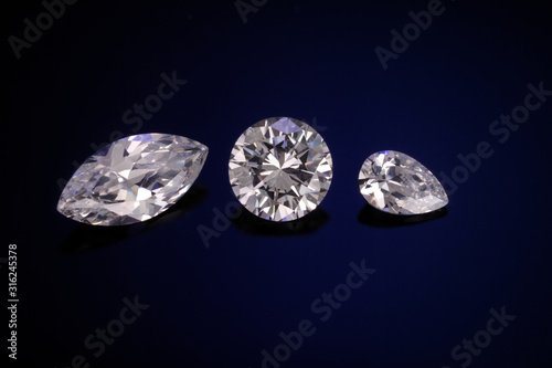 A marque, round and pear cut diamonds sit on a deep blue sandblasted glass reflective background.