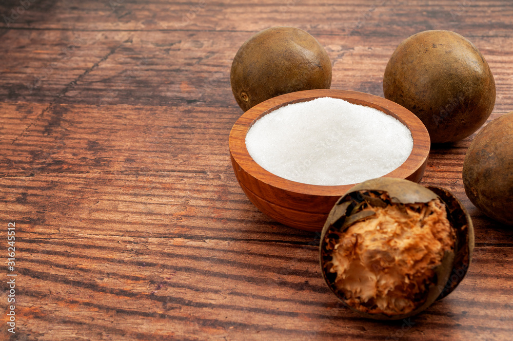 Low calorie alternative to sugar and natural remedy to inflammatory disease and arthritis concept with Luo Han Guo or monk fruit and bowl of sweetener isolated on wood background with copy space Low calorie alternative to sugar and natural remedy to inflammatory disease and arthritis concept with Luo Han Guo or monk fruit and bowl of sweetener isolated on wood background with copy space