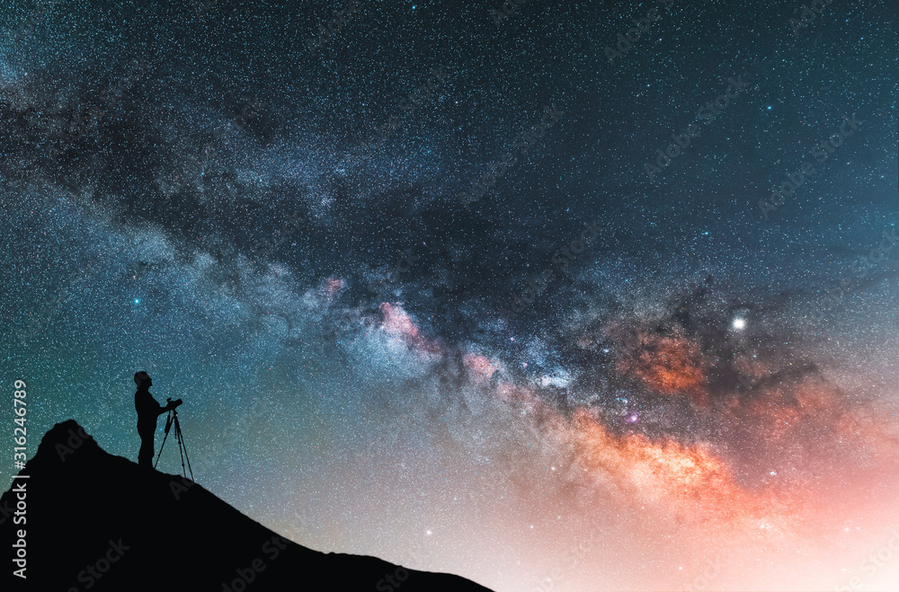 Beautiful starry night landscape. A silhouette of a photographer stands on a hill and looks at a beautiful starry sky with a bright milky way.