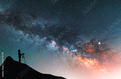 Beautiful starry night landscape. A silhouette of a photographer stands on a hill and looks at a beautiful starry sky with a bright milky way.