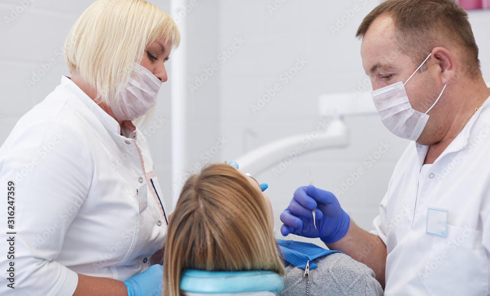 Fototapeta premium Doctor dentist treats teeth of a beautiful young girl patient. The girl on reception at the dentist. Doctor dentist treats tooth