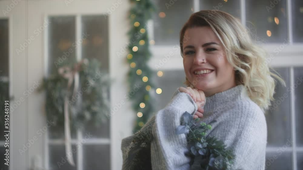 Woman in warm sweater laughs with christmas wreath in her hands, decorating the scandinavian interior for christmas, cozy new year's home atmosphere, Full HD 120fps Prores HQ