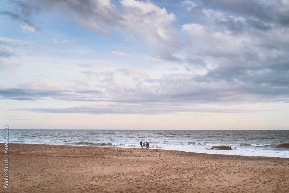 A group of young people watch the waves on Ramsgate main sands beach on a windy winter day in Kent.