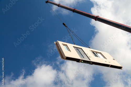 Component for a prefabricated house is transported from an orange jib of a mobile crane at a great height for assembly