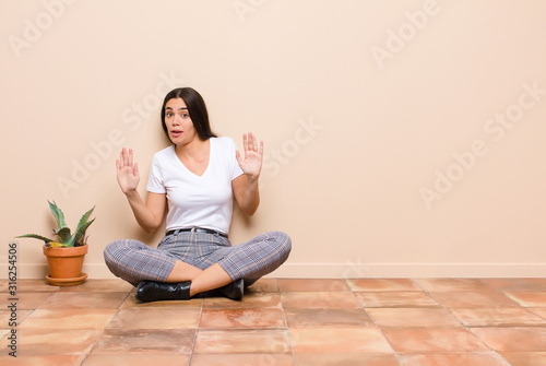 young pretty woman looking nervous, anxious and concerned, saying not my fault or I didn‚Äôt do it sitting on a floor photo