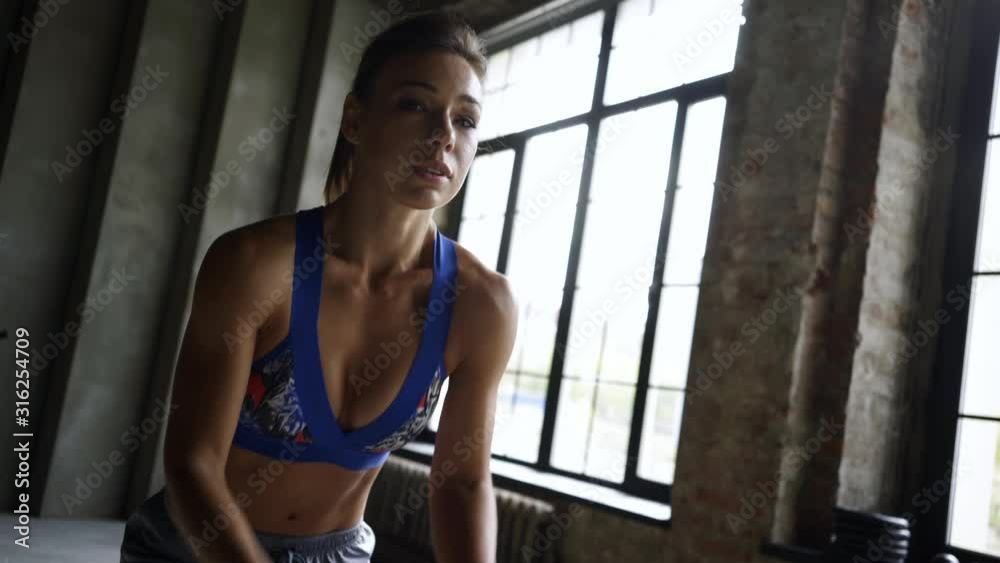 Fitness girl exercising with battle ropes at gym. Handheld shot, close-up portrait woman training doing battling rope workout working out arms and cardio for cross fit exercises in interior