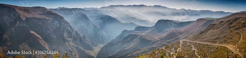 Beautiful panoramic view from the top of tatev gorge while the famous longest cable car Wings of Tatev and small village. South Armenian autumn landscape with Caucasus mountain range and foggy canyon