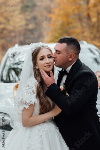 Happy groom kisses his gorgeous bride. Beautiful couple in their wedding day. Happy handsome groom and beautifyl bride hugging. Amazing smiling wedding couple. Pretty bride and stylish groom.