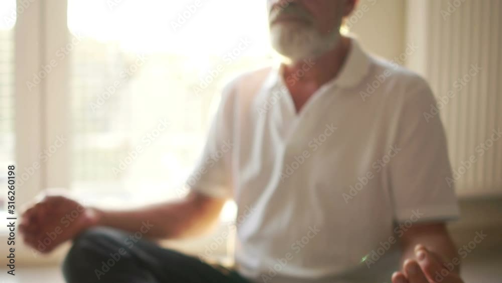 Close portrait of an elderly gray-bearded man sitting on the floor in a lotus position. Yoga classes, spiritual practices, meditation