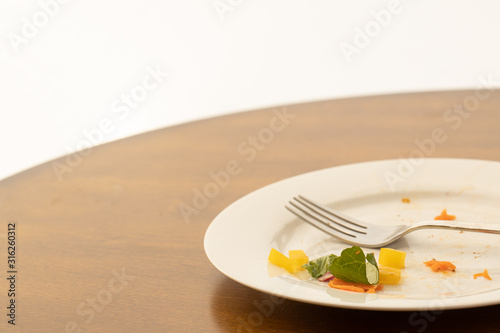 Bits of salad left on a plate on a table with a fork