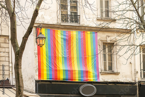 Facade with gay pride flag instead of a window Paris, France. Rainbow flag of the LGBT community as a symbol of love, freedom, equality, rights concepts. photo