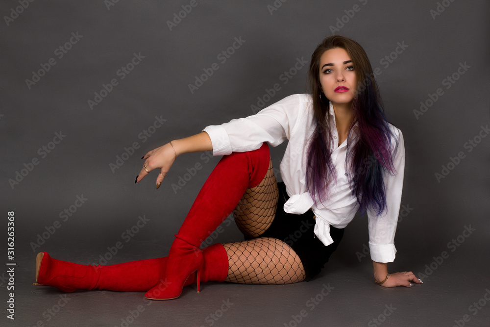 Girl brunette in a white shirt and red boots and stockings in a large mesh on a gray studio background in full height.