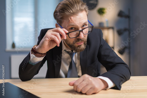 Handsome office clerk at a desk looking at camera with interest over his glasses