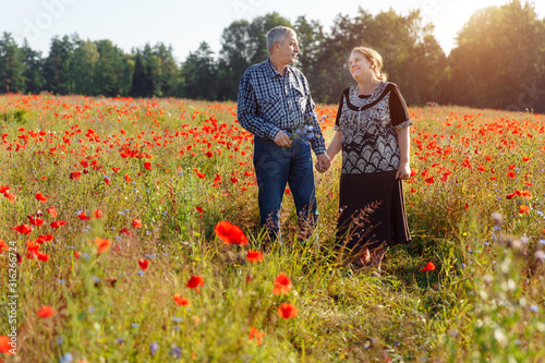 Elderly lovers in a field of flowers. Husband and wife aged outdoors. Senior citizens among poppies.