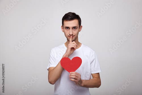A cute young man in a white T-shirt with a red heart in his hands. © Svitlana