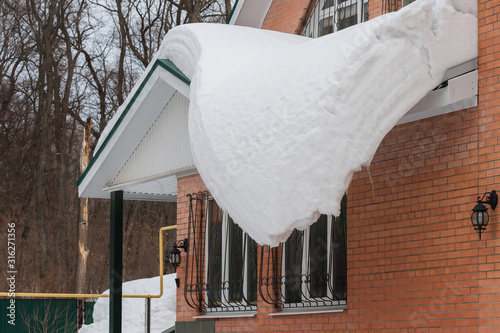 A large layer of snow slowly slides from the roof of the house, it is dangerous