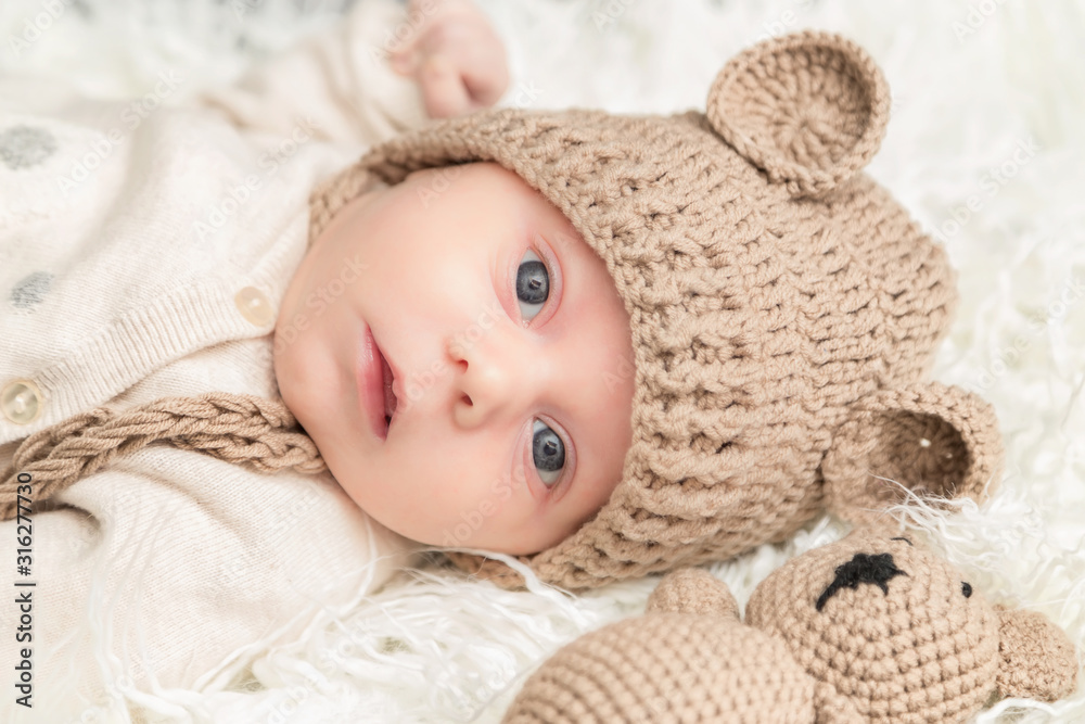 Newborn baby with knitted cap and bear laying white fur background. Baby portrait. Newborn baby with knitted cap and bear laying white fur background. Baby portrait.