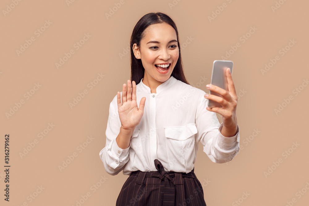 Freestyle. Young woman in shirt standing isolated on bage having video call on smartphone waving to camera friendly talking Freestyle. Young woman in shirt standing isolated on bage having video call on smartphone waving to camera friendly talking