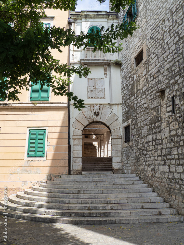 Rincón con una fachada de piedra  un arco en la entrada y escaleras en  Sibenik, Croacia, verano de 2019