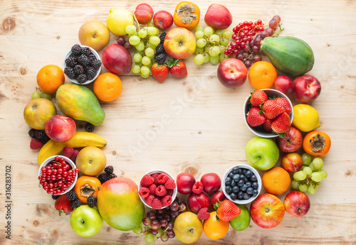 Fototapeta Naklejka Na Ścianę i Meble -  Rainbow fruits frame, strawberries raspberries oranges plums apples kiwis grapes blueberries mango persimmon on light wooden table, top view, copy space for text, selective focus