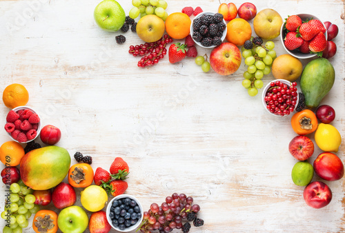 Rainbow fruits background, strawberries raspberries oranges plums apples kiwis grapes blueberries mango persimmon on white wooden table, top view, copy space for text, selective focus photo