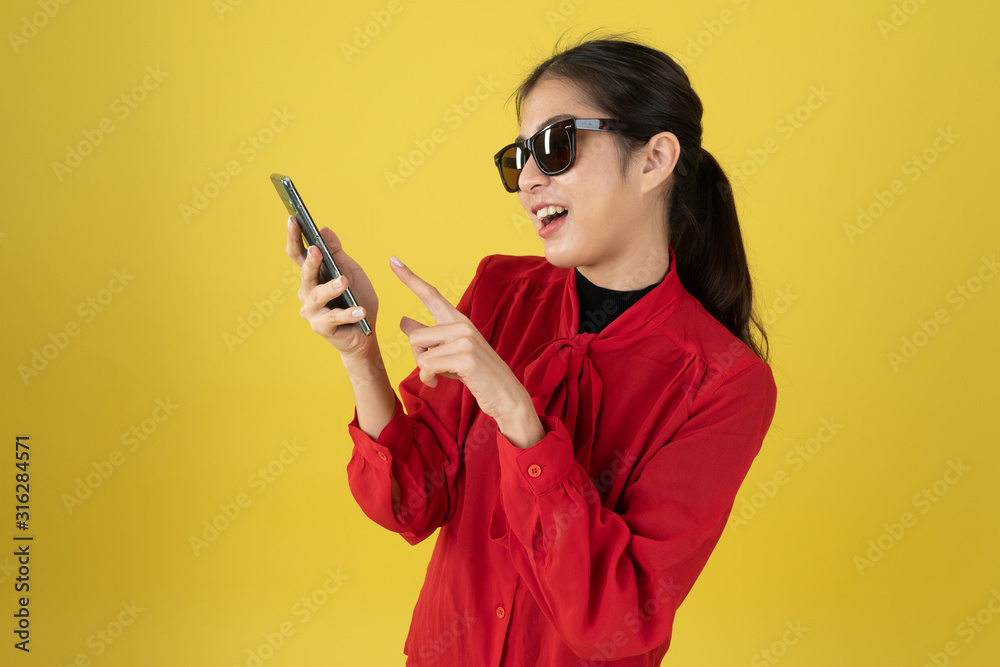 Medium shot of a girl in red shirt, and sunglasses holding mobile. .The photo is made on the yellow background. Medium shot of a girl in red shirt, and sunglasses holding mobile. .The photo is made on the yellow background.