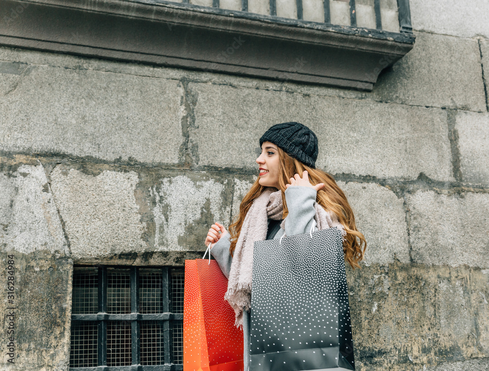 Attractive blonde caucasian girl dressed in scarf and hat carries shopping bags walking on a city street Attractive blonde caucasian girl dressed in scarf and hat carries shopping bags walking on a city street