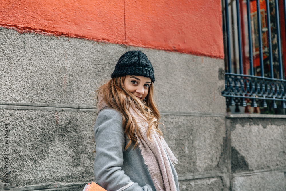 Beautiful young caucasian girl with winter clothes looks at camera smiling on a city street