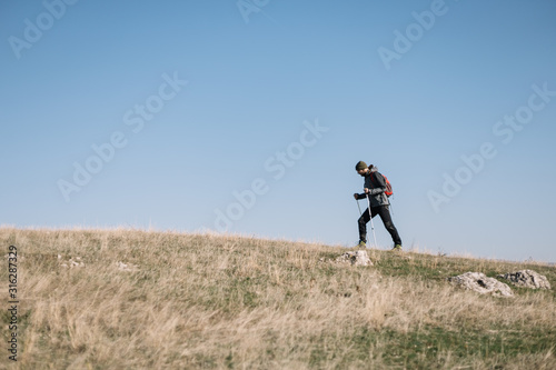 Male hiker walking through green hills and using poles