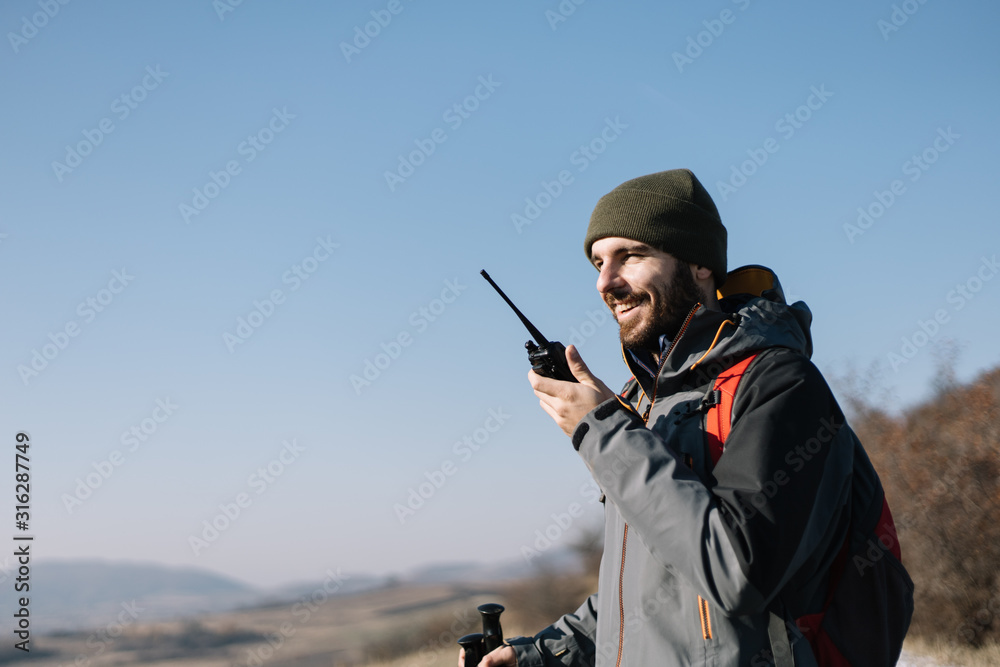 Smiling man speaking on two-way radio for hiking - obrazy, fototapety, plakaty 