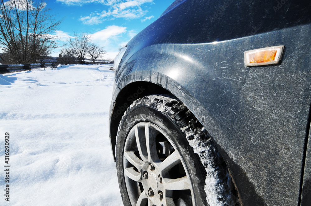 Close-up of a car on the snow near the road with trees against blue sky with clouds
