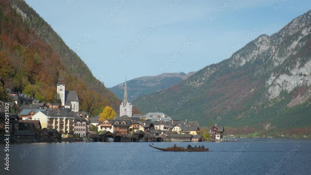 Autumn colors in famous tourist destination idillyc town Hallstatt in Austrian mountains Alps. Cathedral church, local houses, golden leaves on trees on high hills and a boat floating on lake. Autumn colors in famous tourist destination idillyc town Hallstatt in Austrian mountains Alps. Cathedral church, local houses, golden leaves on trees on high hills and a boat floating on lake.